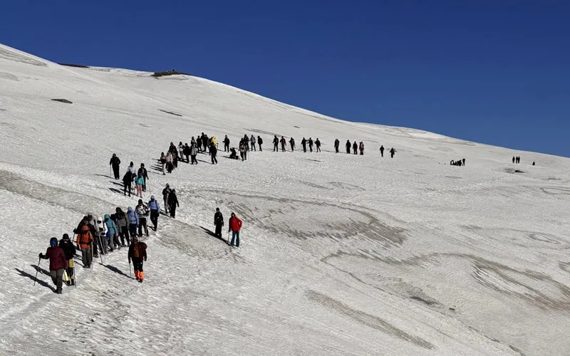 Long line of hikers trekking across an expansive snowfield ascending toward Sar Pass