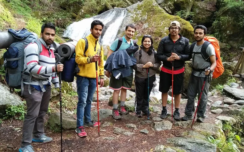 Group of hikers with backpacks standing ready on a forest trail in Tirthan Valley