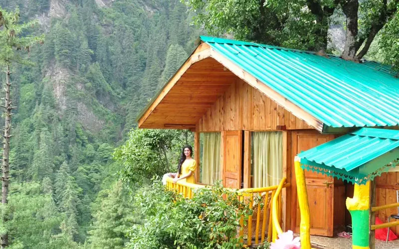 Cozy wooden cottage stay with green and blue roofs set among lush valley hills in Jibhi
